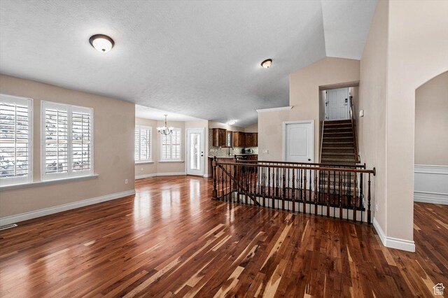 4876 S 1525 E, Ogden, UT 84403 - living room featuring baseboards, dark wood finished floors, vaulted ceiling, arched walkways, and a notable chandelier