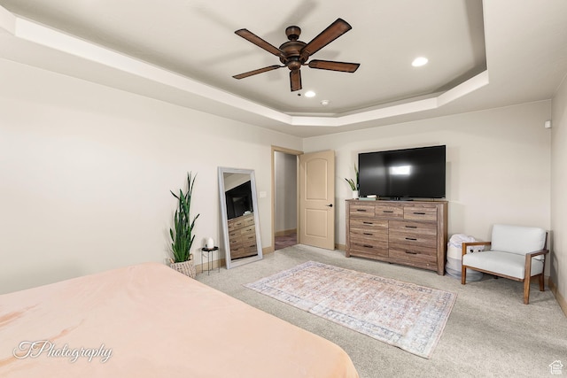 carpeted bedroom with a raised ceiling and ceiling fan