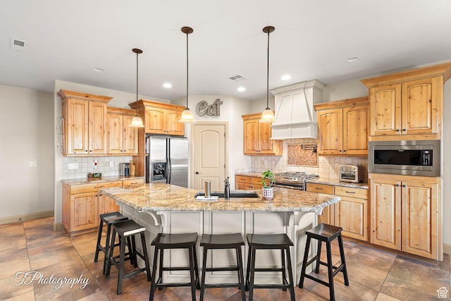 kitchen with pendant lighting, stainless steel appliances, a center island with sink, and custom range hood