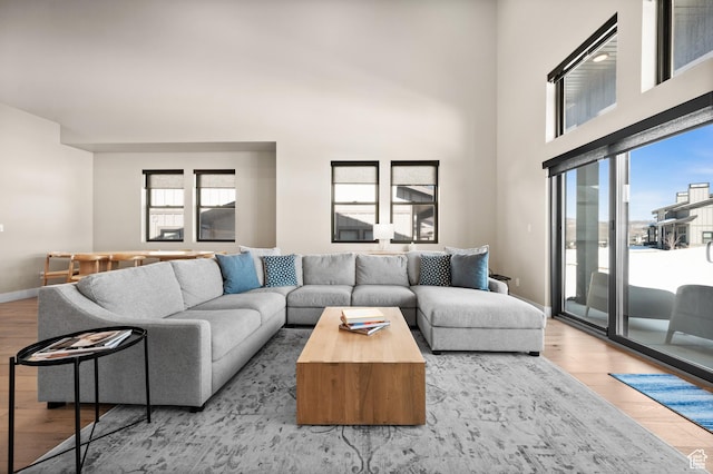 living room with light wood-type flooring, baseboards, and a towering ceiling