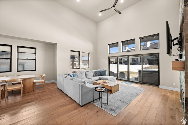 living area with a high ceiling, baseboards, light wood-type flooring, and ceiling fan