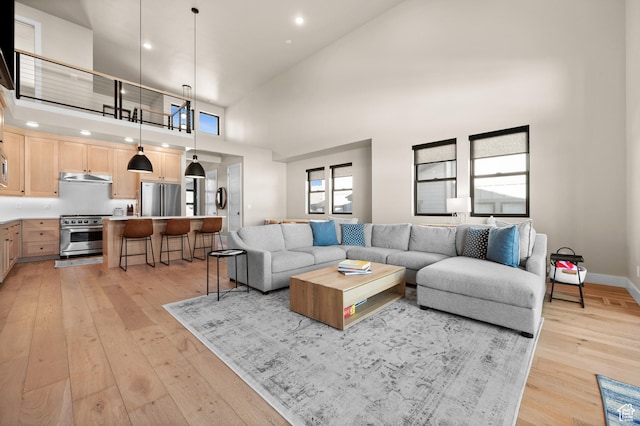 living room featuring a high ceiling, recessed lighting, light wood-style floors, and baseboards