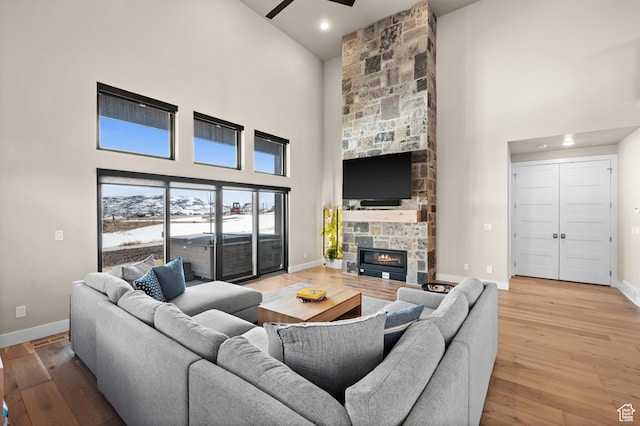 living room featuring light wood finished floors, ceiling fan, a high ceiling, and baseboards