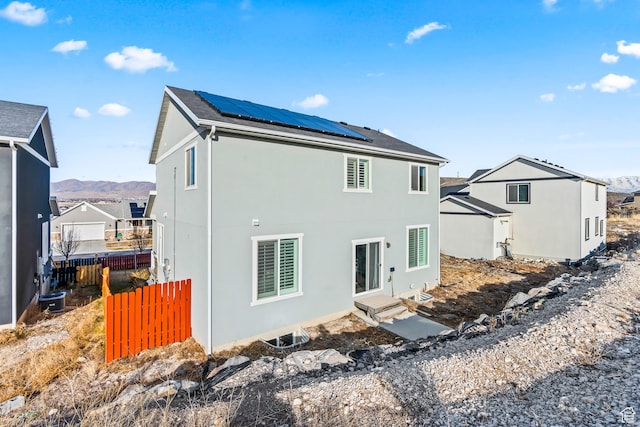 rear view of house with entry steps, fence, solar panels, and stucco siding