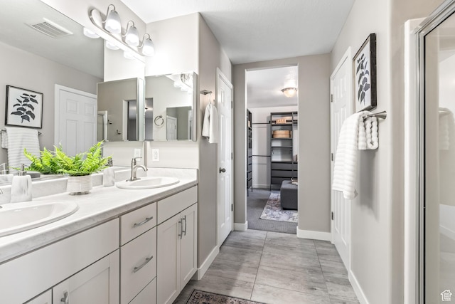 full bath with a sink, visible vents, a shower with door, and double vanity