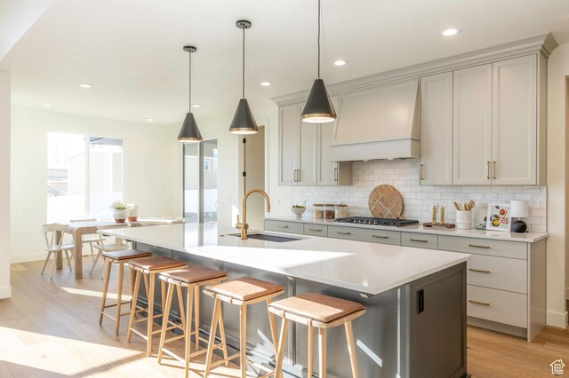 7277 W Hall Crossing Dr S, Herriman, UT 84096 - kitchen featuring custom exhaust hood, a sink, light wood-type flooring, a breakfast bar, and backsplash