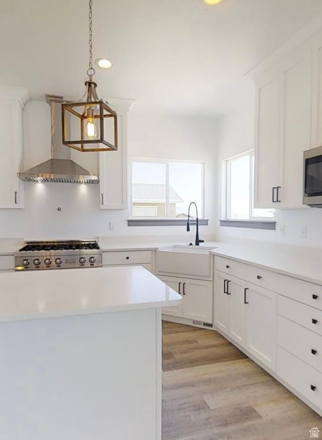 kitchen featuring pendant lighting, appliances with stainless steel finishes, wall chimney exhaust hood, and white cabinets