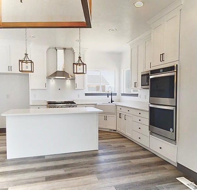 kitchen with white cabinets, appliances with stainless steel finishes, hanging light fixtures, and wall chimney range hood