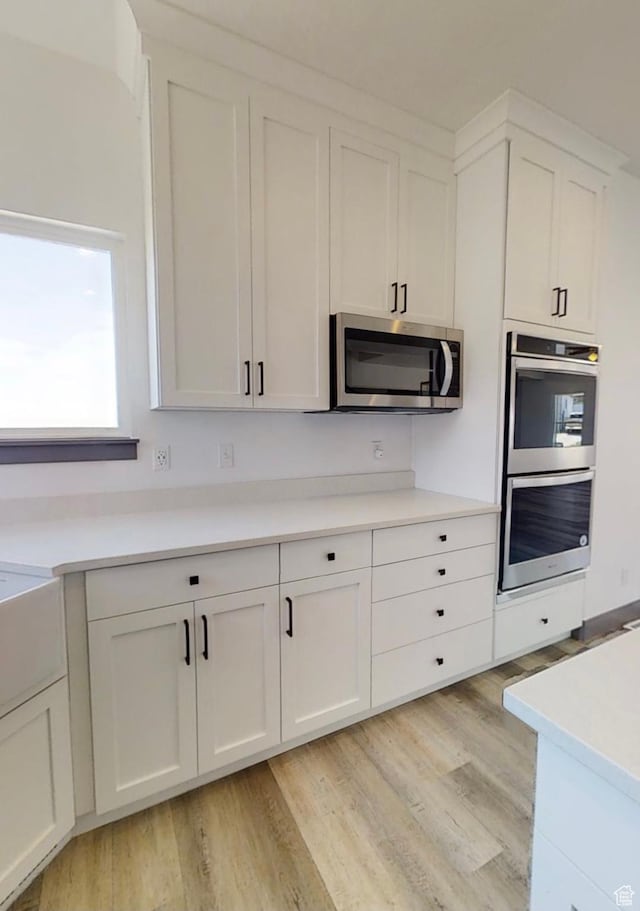 kitchen with white cabinetry, stainless steel appliances, and light wood-type flooring