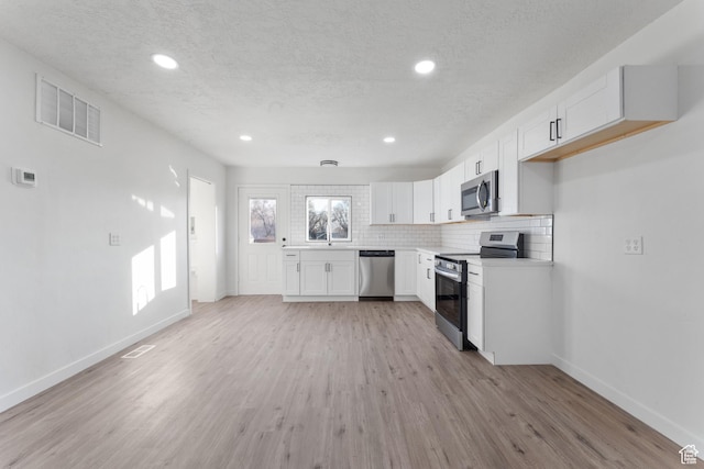 225 8th St, Ogden, UT 84404 - kitchen featuring a textured ceiling, light hardwood / wood-style flooring, tasteful backsplash, white cabinets, and appliances with stainless steel finishes