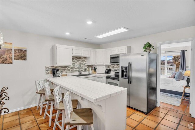 kitchen with tile counters, stainless steel appliances, kitchen peninsula, sink, and white cabinetry