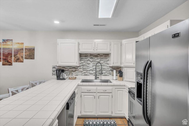 kitchen featuring white cabinets, appliances with stainless steel finishes, and tile countertops