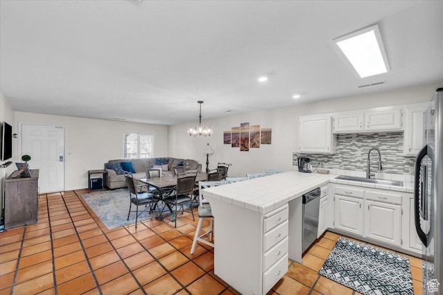 kitchen featuring kitchen peninsula, tile counters, stainless steel appliances, white cabinetry, and sink