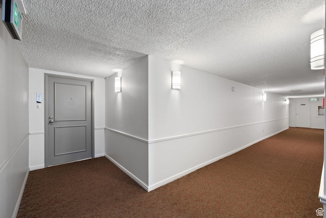 hallway featuring a textured ceiling and dark carpet