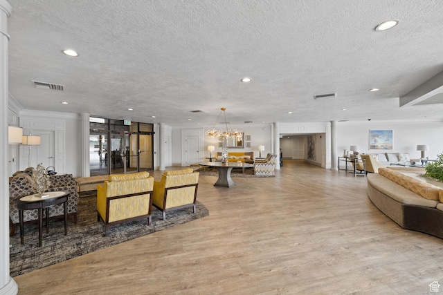 living room with decorative columns, a textured ceiling, a notable chandelier, and ornamental molding