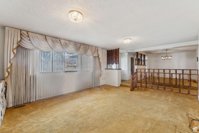 carpeted spare room featuring a textured ceiling and an inviting chandelier