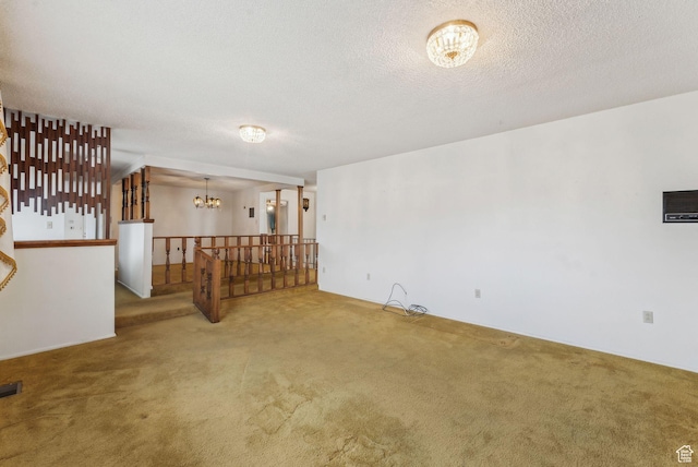 carpeted spare room with a textured ceiling and an inviting chandelier