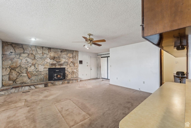 unfurnished living room with carpet flooring, a textured ceiling, ceiling fan, and a wood stove