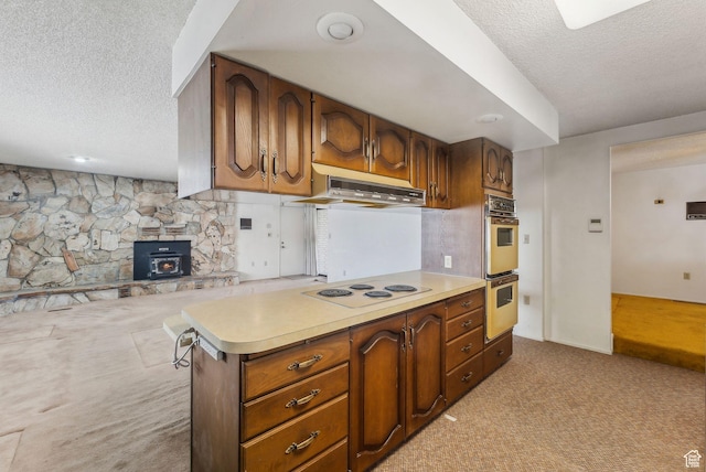 kitchen with a textured ceiling, white electric cooktop, exhaust hood, multiple ovens, and light colored carpet