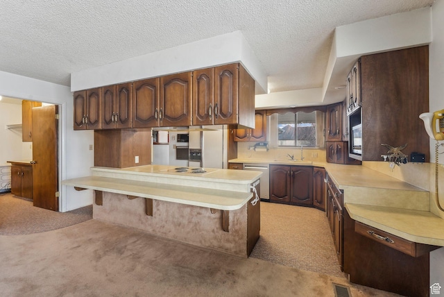 kitchen featuring kitchen peninsula, stainless steel dishwasher, light carpet, a kitchen breakfast bar, and sink