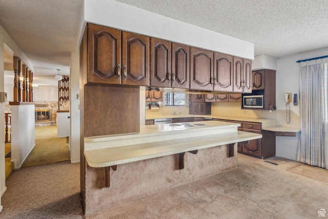 kitchen with a textured ceiling, light colored carpet, kitchen peninsula, and a breakfast bar area
