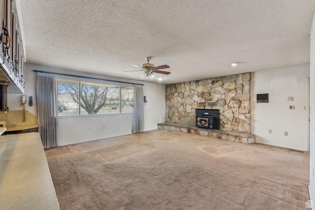 unfurnished living room with a textured ceiling, light carpet, and a wood stove