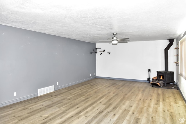 4752 E Max Rd, Downey, ID 83234 - unfurnished living room featuring a textured ceiling, ceiling fan, a wood stove, and light hardwood / wood-style flooring