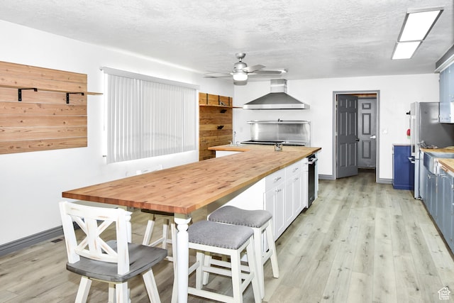 4752 E Max Rd, Downey, ID 83234 - kitchen featuring ceiling fan, stainless steel fridge, butcher block countertops, wall chimney exhaust hood, and blue cabinets