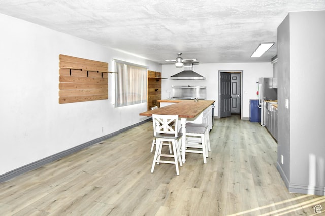 4752 E Max Rd, Downey, ID 83234 - kitchen featuring a breakfast bar area, light hardwood / wood-style floors, ceiling fan, wall chimney exhaust hood, and butcher block counters