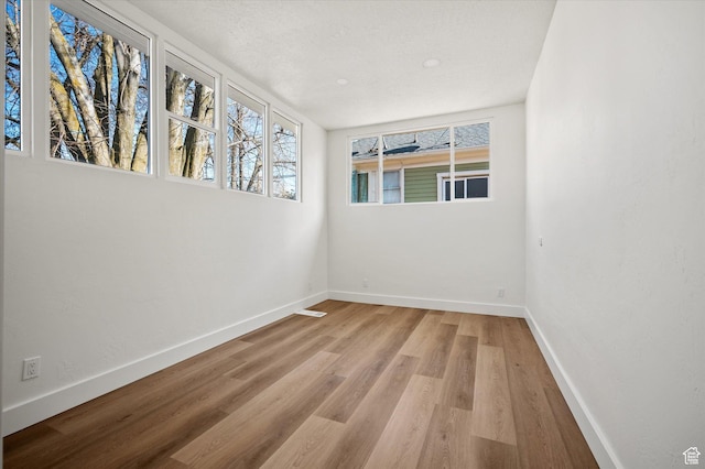 unfurnished room with a textured ceiling, light wood-type flooring, and baseboards
