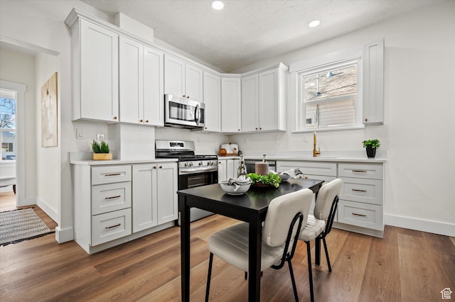 kitchen with white cabinetry, appliances with stainless steel finishes, light countertops, and wood finished floors