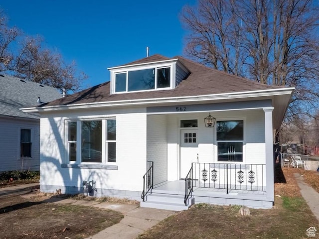 bungalow-style house featuring a porch, roof with shingles, and brick siding