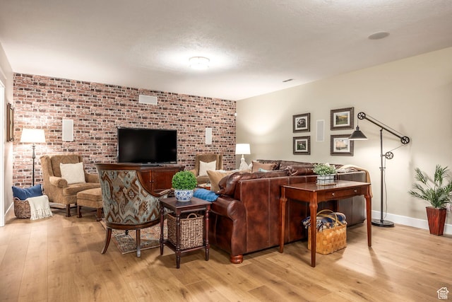 living area featuring a textured ceiling, brick wall, baseboards, and light wood-style floors