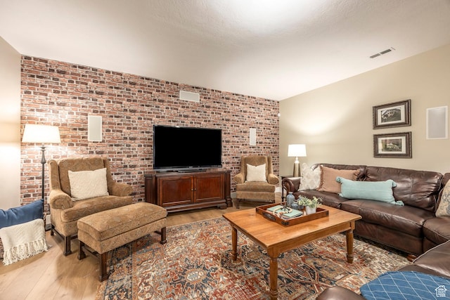 living area featuring visible vents, a textured ceiling, light wood-style flooring, and brick wall