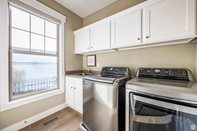 washroom with wood finished floors, visible vents, washing machine and clothes dryer, cabinet space, and a sink