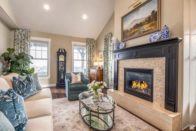living area featuring baseboards, vaulted ceiling, a stone fireplace, recessed lighting, and wood finished floors