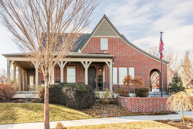 tudor-style house featuring brick siding, covered porch, and a front lawn