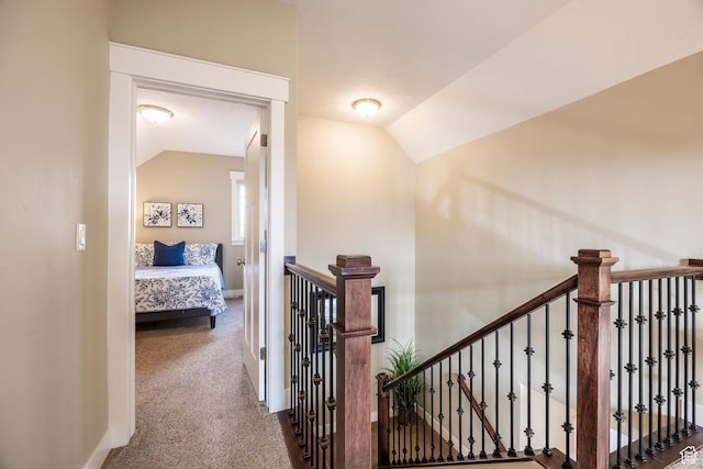 hall featuring vaulted ceiling, an upstairs landing, baseboards, and carpet floors