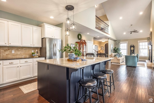 kitchen featuring a center island, dark wood-type flooring, a kitchen bar, freestanding refrigerator, and white cabinetry