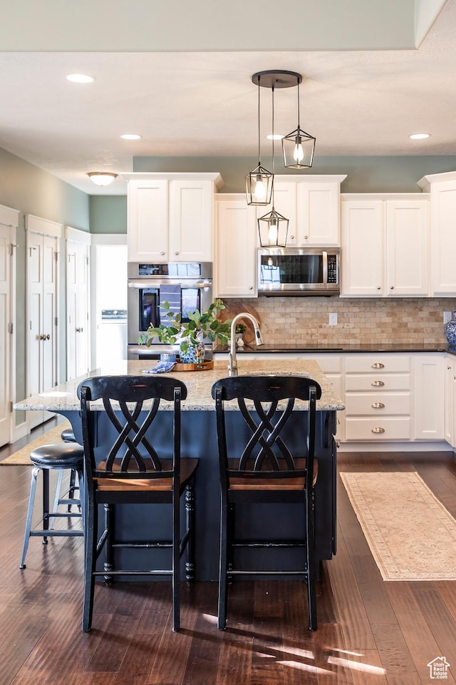 kitchen with tasteful backsplash, stainless steel microwave, a center island with sink, a breakfast bar, and dark wood-style flooring