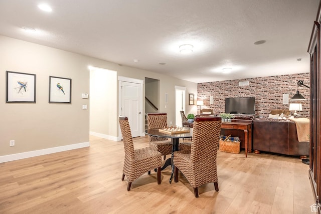 dining space featuring brick wall, baseboards, stairway, light wood-style floors, and a textured ceiling