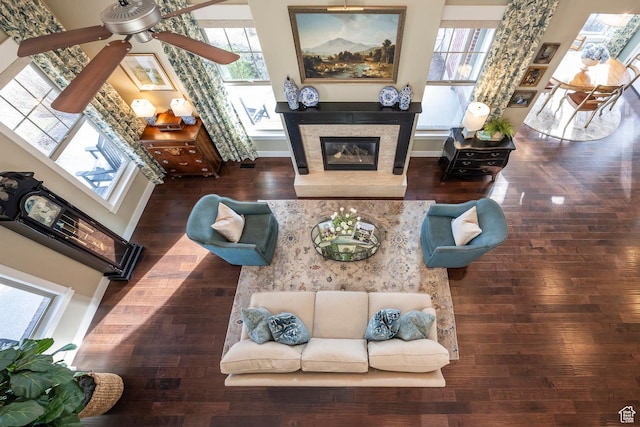 living room featuring a glass covered fireplace, baseboards, wood finished floors, and a ceiling fan