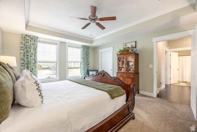 carpeted bedroom featuring a ceiling fan, a raised ceiling, crown molding, and baseboards