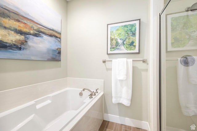 full bathroom featuring a bath, a shower stall, and baseboards