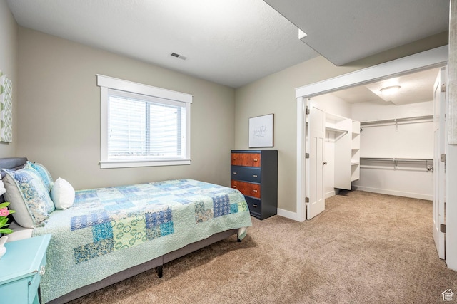 carpeted bedroom featuring a spacious closet, visible vents, and baseboards