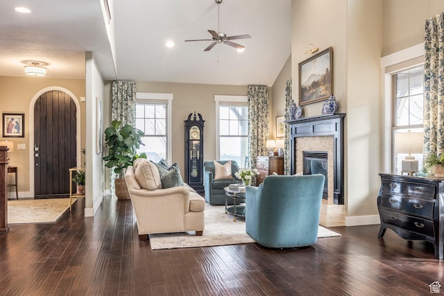 living area with a glass covered fireplace, wood finished floors, a ceiling fan, and high vaulted ceiling