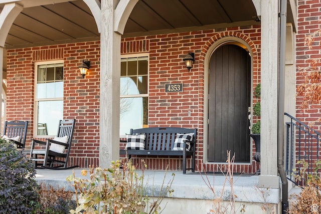 view of exterior entry featuring a porch and brick siding