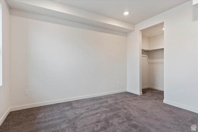 unfurnished bedroom featuring recessed lighting, baseboards, a spacious closet, and dark carpet
