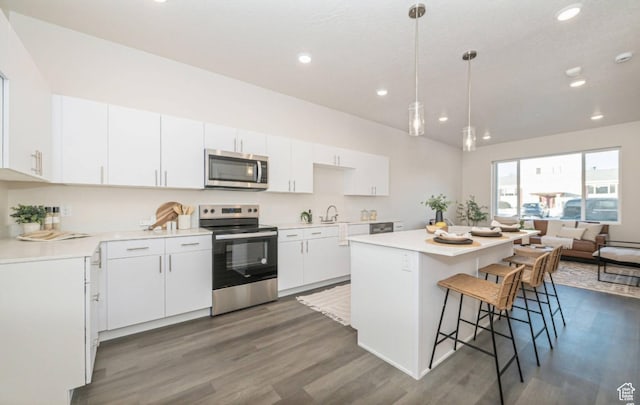 kitchen featuring a kitchen island, dark wood-type flooring, a breakfast bar area, stainless steel appliances, and white cabinetry
