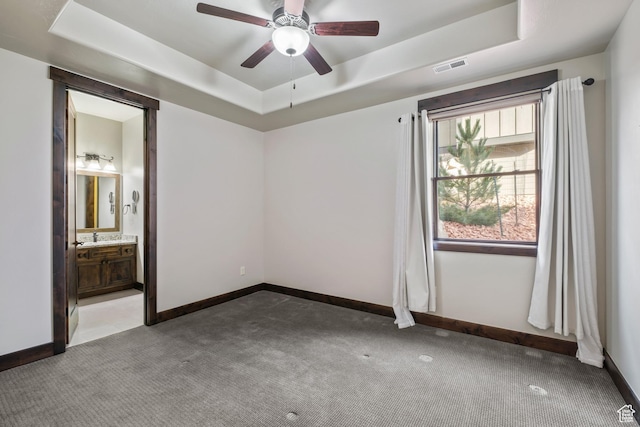unfurnished bedroom with ceiling fan, connected bathroom, a raised ceiling, and carpet floors